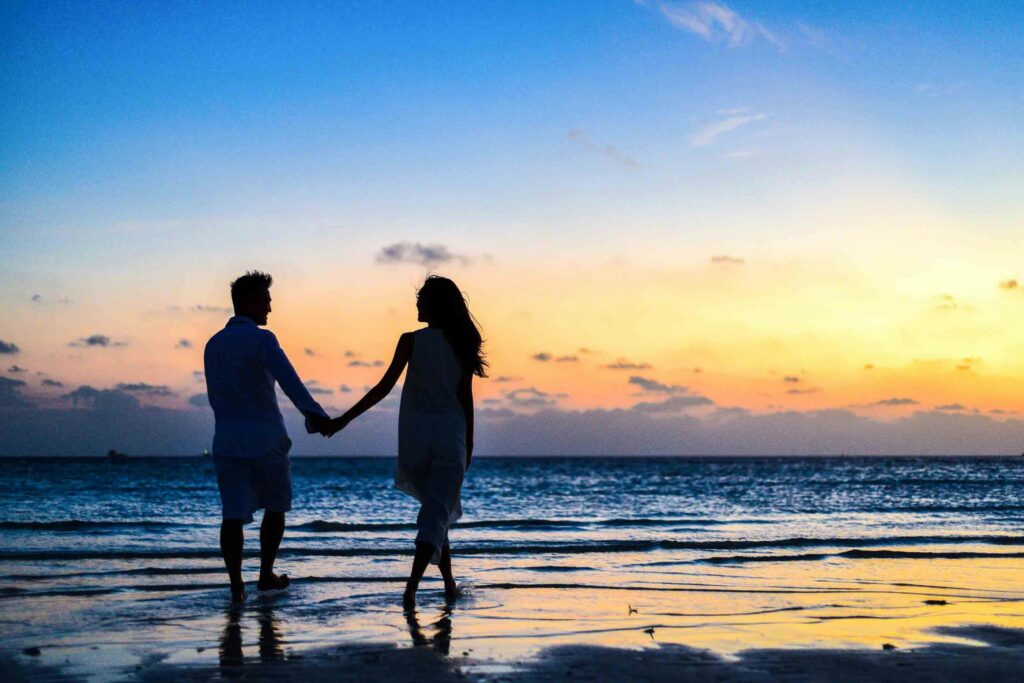pexels-photo-1024960-1024960 A romantic couple walks hand in hand on a tropical beach at sunset, enjoying a serene moment together.